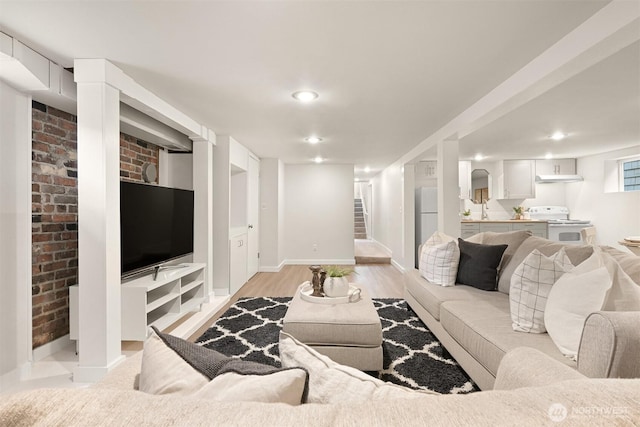 living area featuring baseboards, brick wall, stairs, light wood-style floors, and recessed lighting