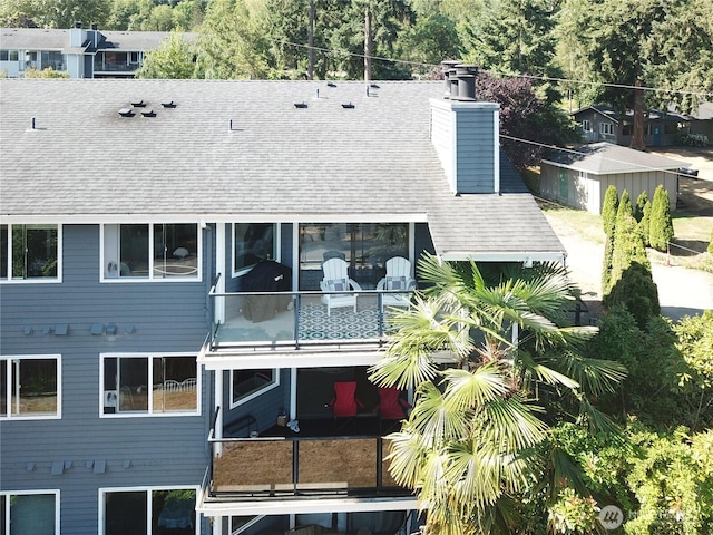 back of house with a balcony, a chimney, and roof with shingles