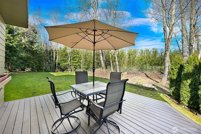 wooden terrace with outdoor dining space, a lawn, and a view of trees