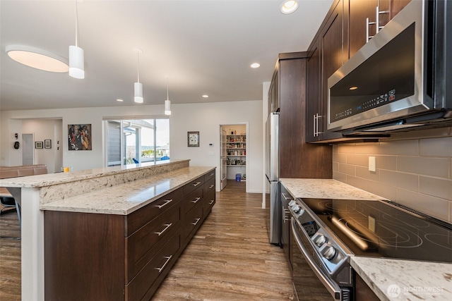 kitchen featuring dark brown cabinets, a center island, light stone countertops, appliances with stainless steel finishes, and wood finished floors