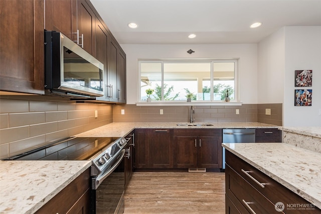 kitchen with dark brown cabinets, light wood-type flooring, light stone counters, stainless steel appliances, and a sink