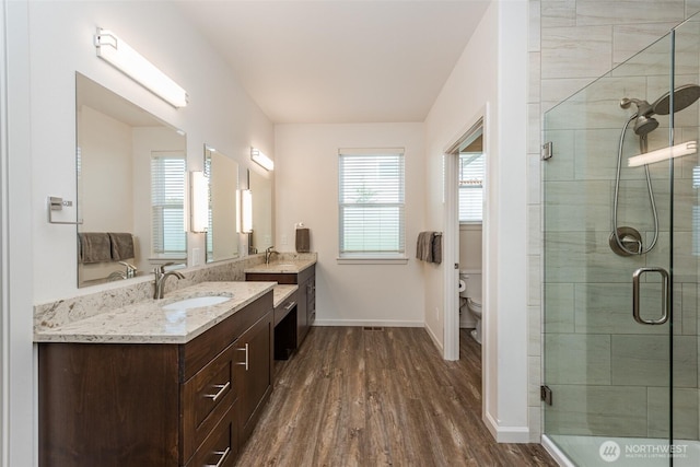 full bath featuring a shower stall, two vanities, wood finished floors, and a sink