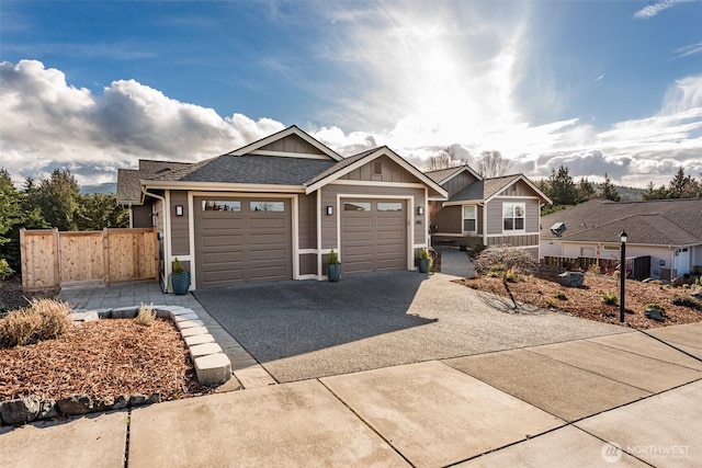 view of front facade featuring an attached garage, board and batten siding, fence, roof with shingles, and driveway