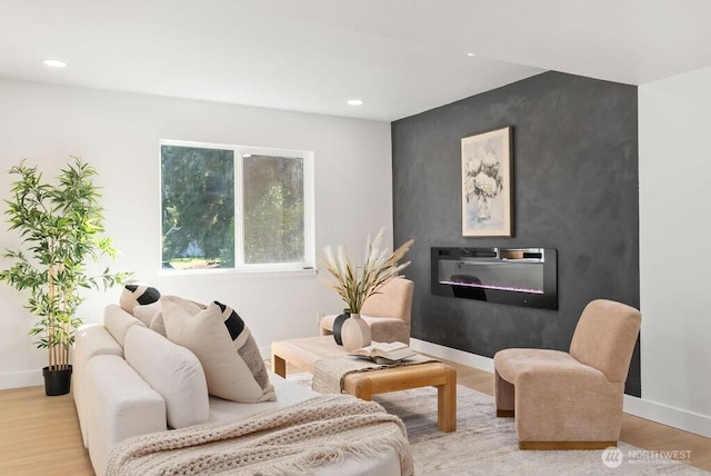 living room with recessed lighting, an accent wall, wood finished floors, baseboards, and a glass covered fireplace
