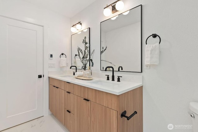 bathroom with marble finish floor, double vanity, a sink, and toilet