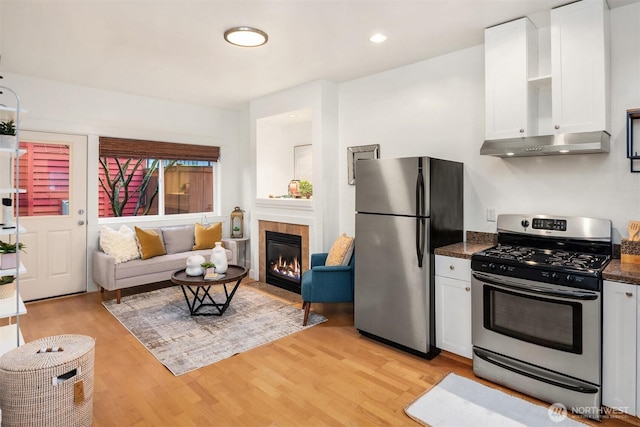 kitchen with wall chimney range hood, white cabinets, light wood-style floors, and appliances with stainless steel finishes