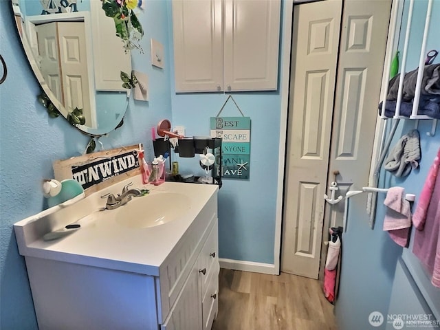 bathroom featuring a textured wall, baseboards, wood finished floors, and vanity