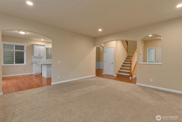 unfurnished living room featuring stairs, arched walkways, light colored carpet, and recessed lighting