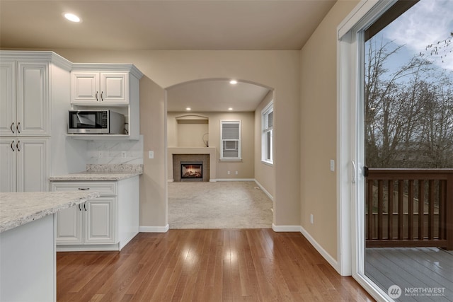 kitchen featuring arched walkways, stainless steel microwave, light wood-style flooring, white cabinetry, and baseboards