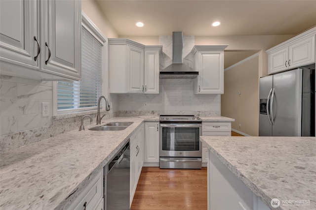 kitchen featuring stainless steel appliances, a sink, backsplash, wall chimney exhaust hood, and light wood finished floors