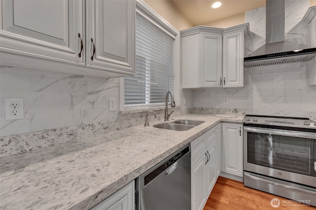 kitchen featuring light wood finished floors, backsplash, appliances with stainless steel finishes, a sink, and wall chimney exhaust hood