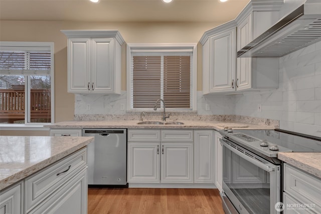 kitchen featuring white cabinets, stainless steel appliances, light wood-type flooring, wall chimney range hood, and a sink