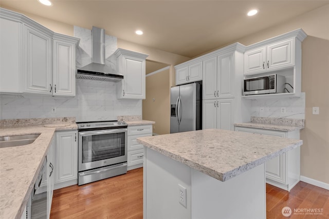 kitchen with light wood finished floors, stainless steel appliances, wall chimney range hood, and white cabinetry