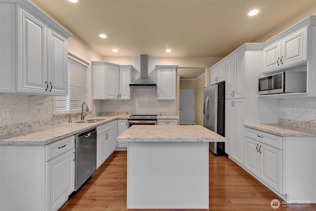 kitchen with a sink, white cabinets, appliances with stainless steel finishes, wall chimney exhaust hood, and light wood finished floors