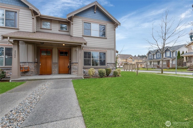 view of front of home with stone siding, a residential view, covered porch, a front yard, and a shingled roof