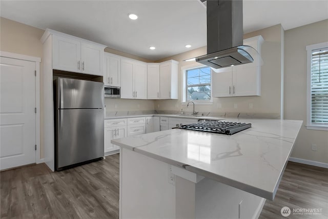 kitchen featuring island exhaust hood, stainless steel appliances, a peninsula, and white cabinetry