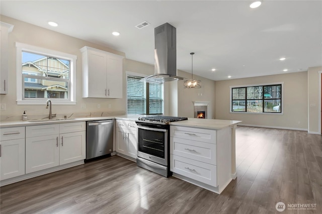 kitchen with visible vents, a peninsula, island exhaust hood, a sink, and stainless steel appliances