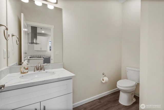 half bathroom featuring vanity, toilet, wood finished floors, and baseboards