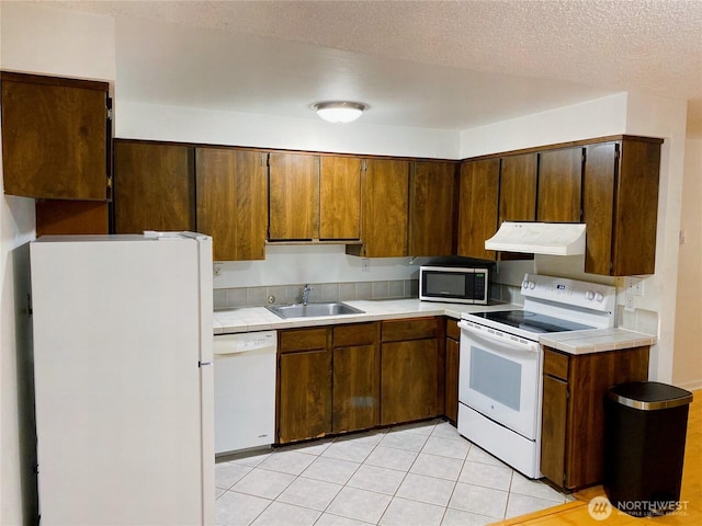 kitchen featuring white appliances, tile countertops, a textured ceiling, under cabinet range hood, and a sink