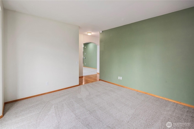 carpeted spare room featuring arched walkways and baseboards