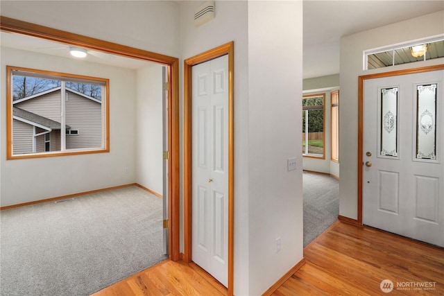 foyer with light wood-type flooring, light colored carpet, visible vents, and baseboards