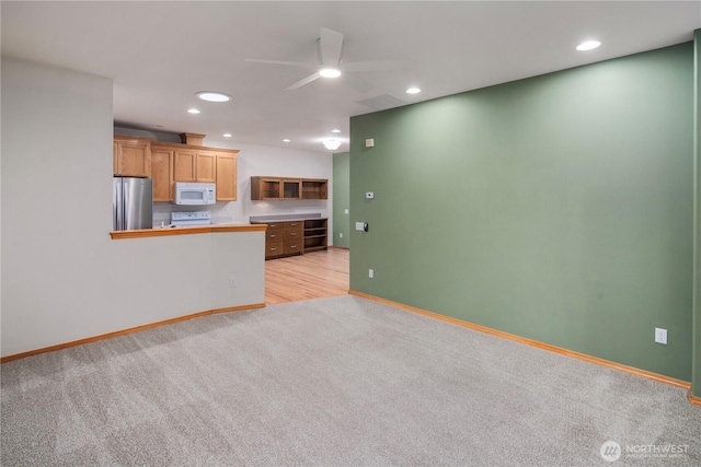 kitchen with baseboards, light colored carpet, white microwave, stove, and freestanding refrigerator