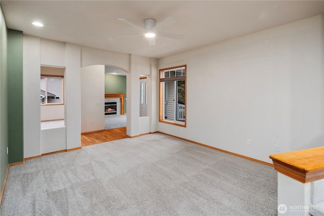 unfurnished living room with carpet floors, a ceiling fan, baseboards, and a tiled fireplace