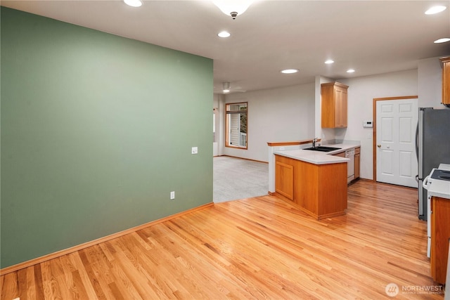 kitchen featuring light wood finished floors, recessed lighting, white dishwasher, a sink, and a peninsula