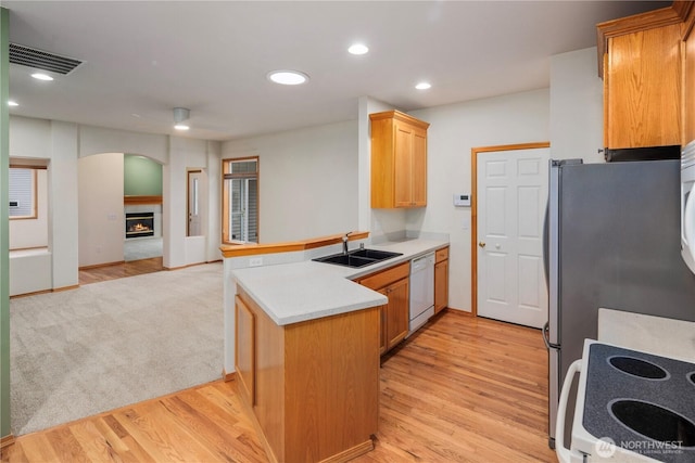 kitchen featuring white dishwasher, a peninsula, a sink, visible vents, and a glass covered fireplace