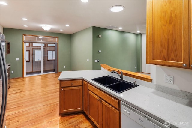 kitchen with light countertops, light wood finished floors, white dishwasher, and a sink