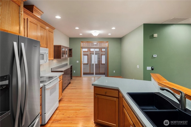 kitchen with light wood finished floors, recessed lighting, light countertops, a sink, and white appliances