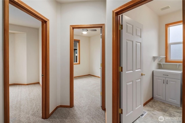 corridor featuring baseboards, visible vents, and light colored carpet