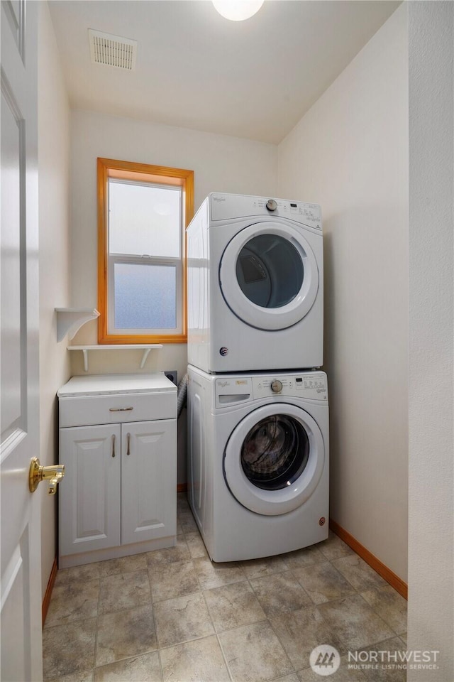 laundry room with stacked washer and dryer, cabinet space, visible vents, and baseboards