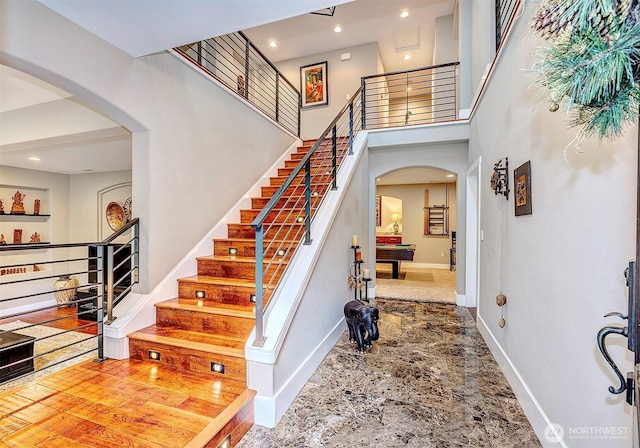 staircase with arched walkways, pool table, a high ceiling, and baseboards