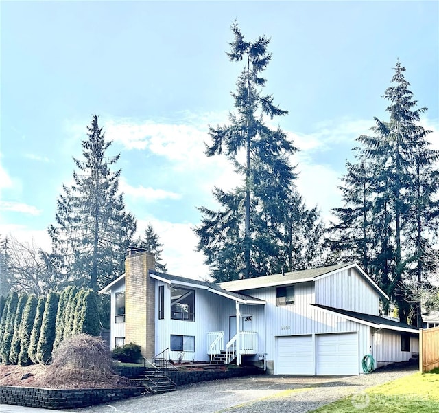 raised ranch with aphalt driveway, a chimney, and a garage