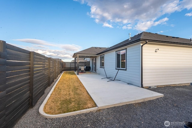 view of home's exterior featuring a fenced backyard, a shingled roof, and a patio