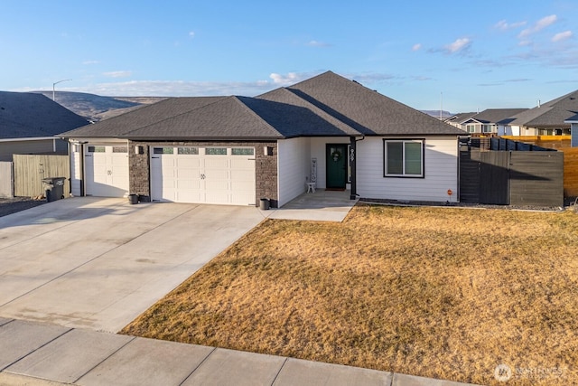 ranch-style home featuring roof with shingles, concrete driveway, fence, a garage, and a front lawn