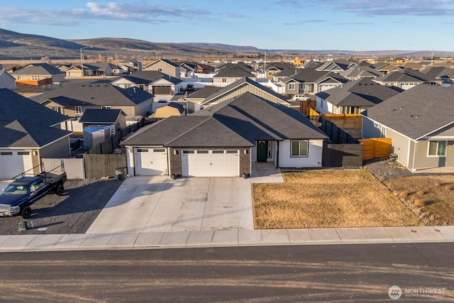 view of front of house featuring a garage, concrete driveway, a residential view, fence, and a mountain view