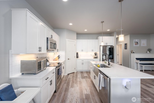 kitchen with appliances with stainless steel finishes, light wood-style floors, a sink, and backsplash