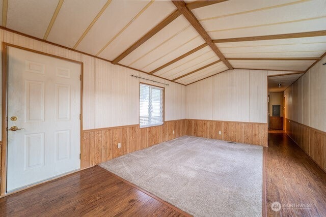 empty room with wooden walls, vaulted ceiling, wood finished floors, and wainscoting