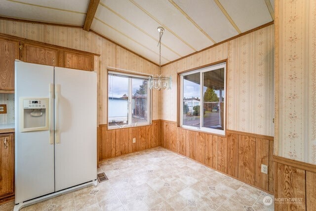 kitchen with lofted ceiling with beams, wainscoting, wooden walls, white fridge with ice dispenser, and wallpapered walls