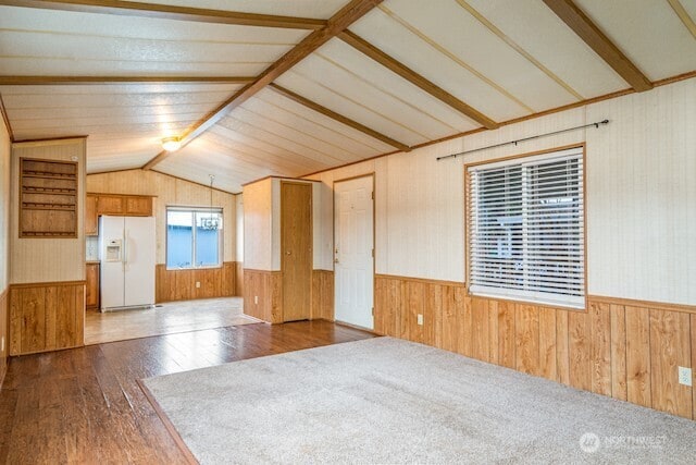 empty room featuring vaulted ceiling with beams, a wainscoted wall, wooden walls, and hardwood / wood-style floors