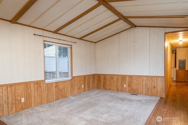 empty room featuring vaulted ceiling with beams, wood walls, and wainscoting