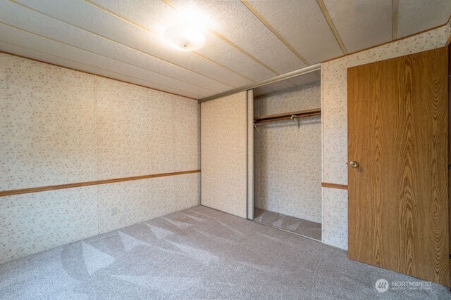 unfurnished bedroom with a closet, carpet flooring, and wallpapered walls