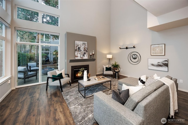 living room featuring a healthy amount of sunlight, a high ceiling, dark wood-type flooring, and a glass covered fireplace