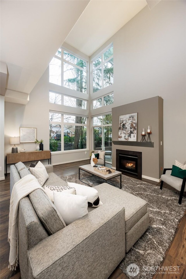 living area featuring a towering ceiling, baseboards, wood finished floors, and a glass covered fireplace