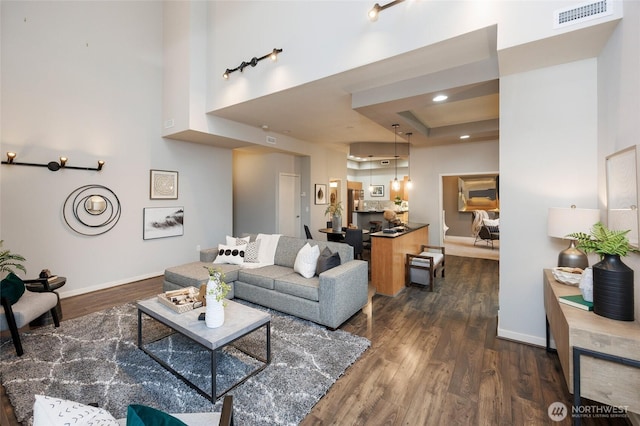 living area with baseboards, visible vents, dark wood-type flooring, a high ceiling, and recessed lighting