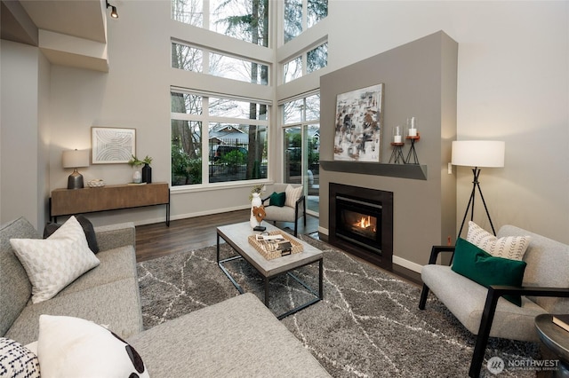 living room with a high ceiling, baseboards, wood finished floors, and a glass covered fireplace