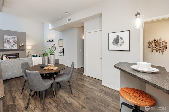 dining area featuring dark wood-type flooring, a fireplace, visible vents, and baseboards