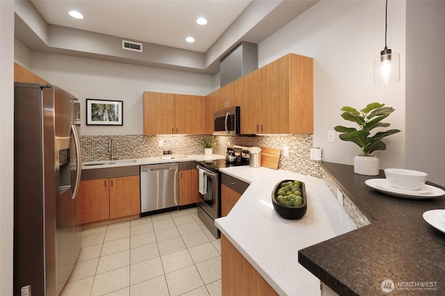 kitchen featuring tasteful backsplash, visible vents, brown cabinetry, appliances with stainless steel finishes, and a sink